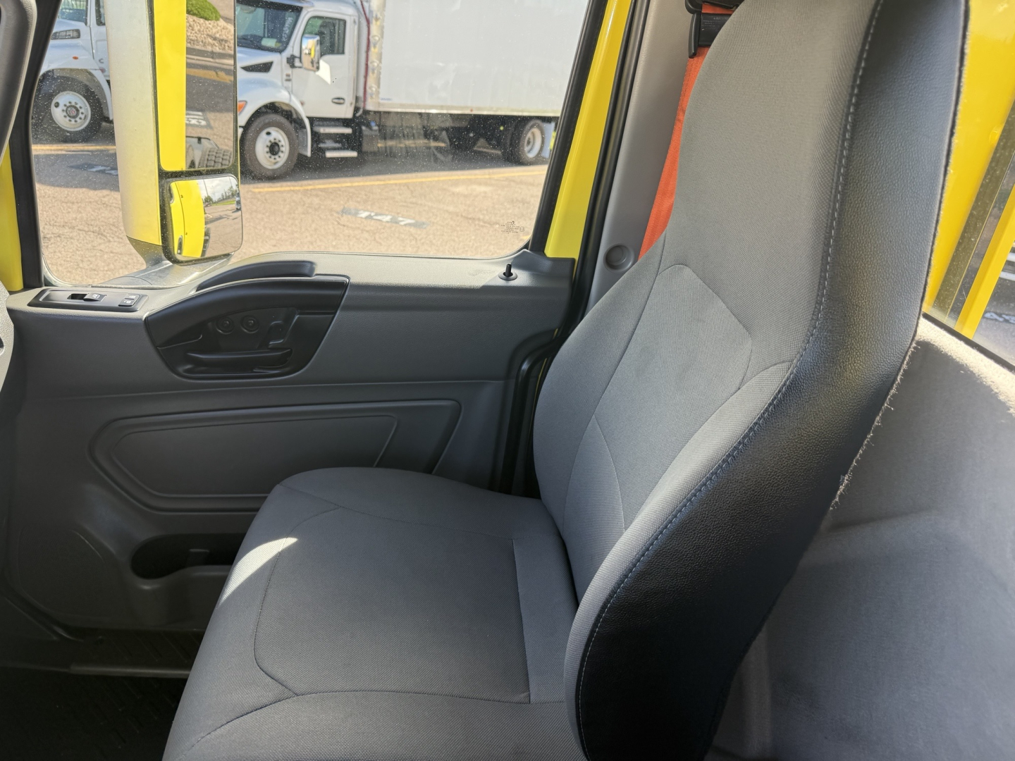 Interior of a 2023 International LT625 cab showing grey driver's seat and door panel; yellow exterior visible through window; partial dashboard controls.