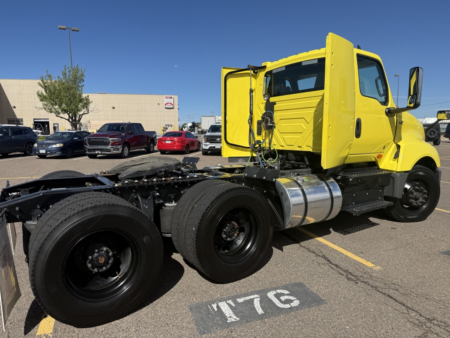 Truck chassis and cab of a yellow 2023 International LT625 in a dealership lot, side view showing cab, wheels, and fuel tanks.
