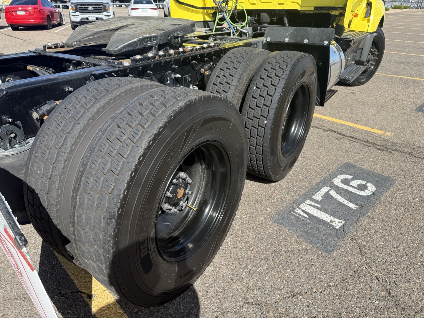 Truck chassis with dual rear axles showing tires, fuel tanks, and parts of a yellow International LT cab in a parking lot.