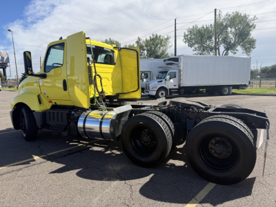 Vehicle side view of a yellow 2023 International LT625 conventional daycab truck chassis shown with dual rear axles and fuel tanks.