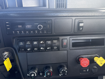 Trucks cab interior showing dashboard controls and ignition with yellow tag. AM/FM radio display and various switches and knobs. Red and yellow hazard/parking brake knobs visible.