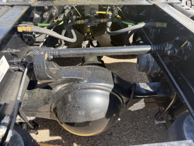 Engine bay showing driveline and suspension components under a 2023 International LT625 cab. Visible air lines, hoses, and transfer case housing.