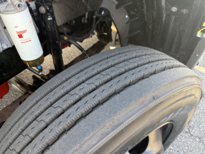 Truck wheel and suspension area with dual tires, fuel filter canister, and hydraulic lines visible under a 2023 International LT625 cab; shows treaded heavy-duty tire
