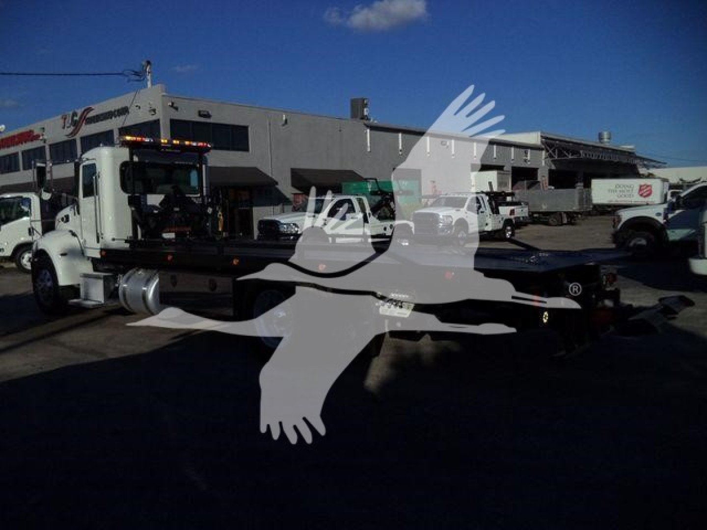 Peterbilt rollback truck in a lot with other vehicles; faint watermark overlay.