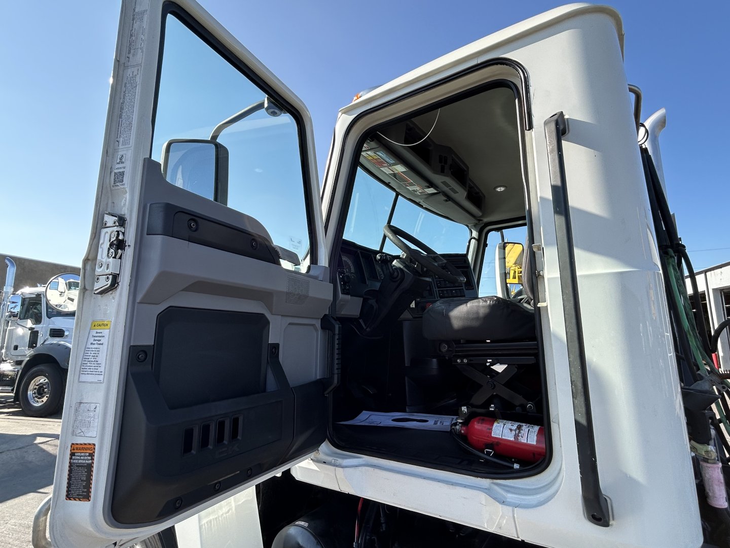 Cab interior of a 2020 Mack PI64T truck with door open, showing steering wheel, seat, dashboard, and a fire extinguisher in the doorway.
