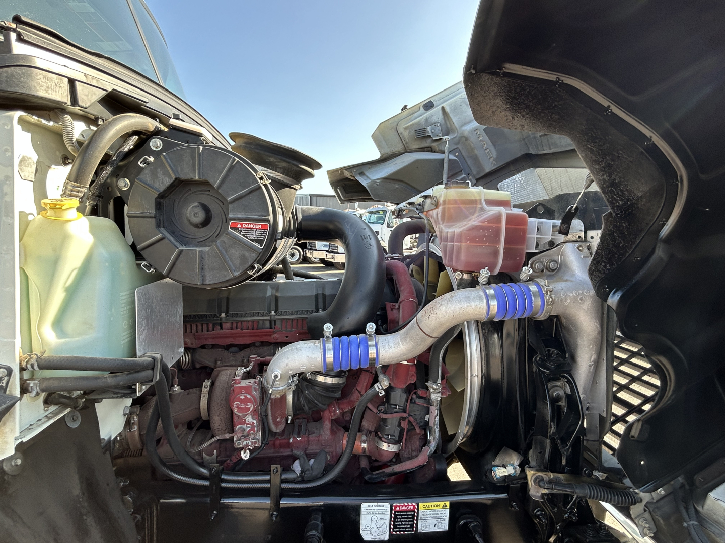 Mack PI64T engine bay showing coolant reservoir, intake piping, hoses, and turbocharger components.