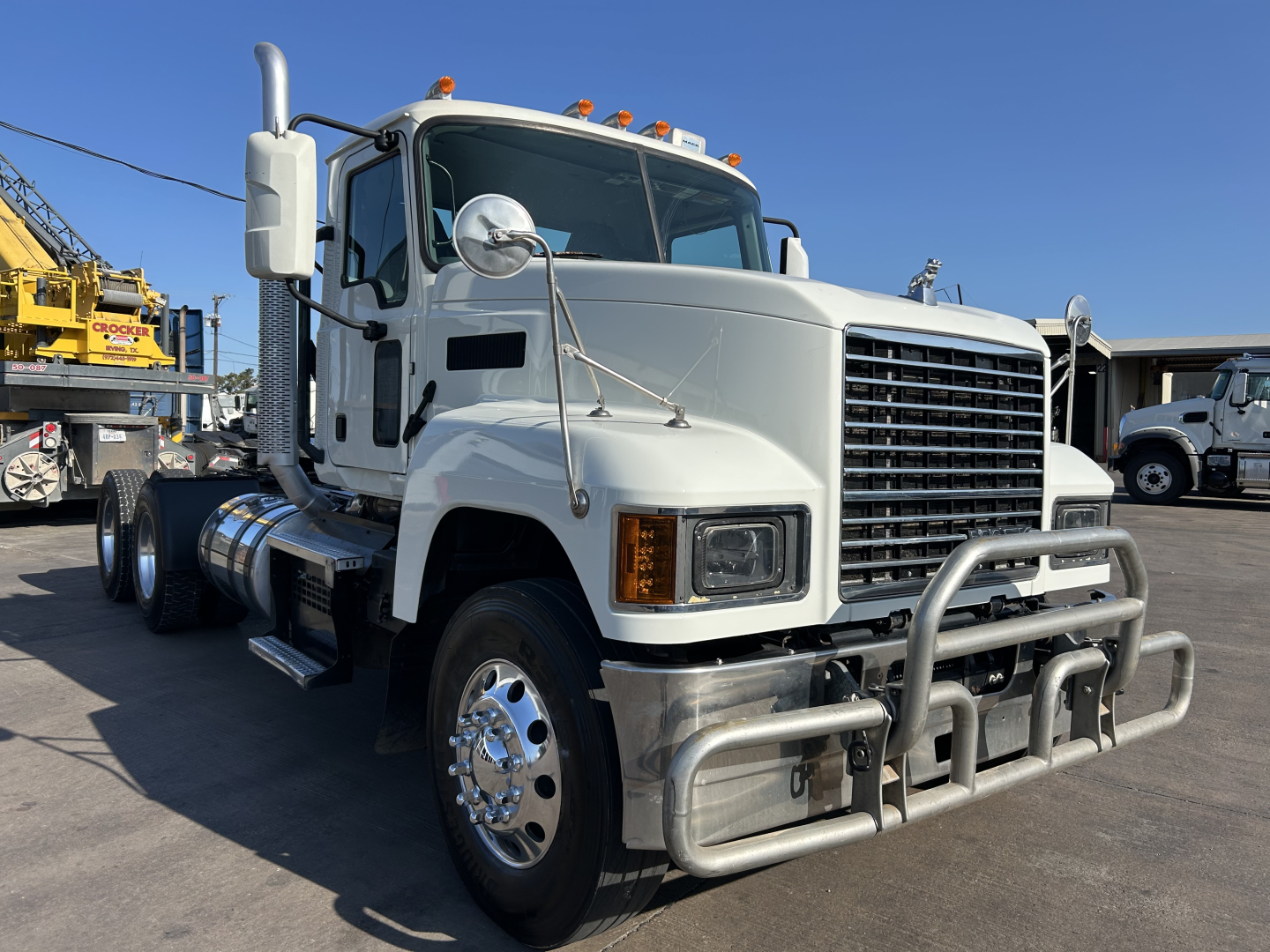 Truck image: 2020 Mack PI64T conventional daycab front-left view, white cab, chrome bumper guard, large grille, dual rear dual wheels, fuel tanks, and side mirrors.