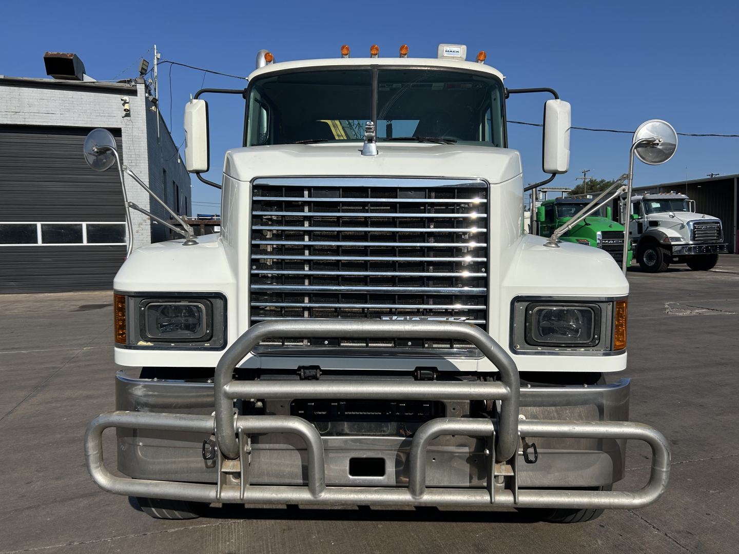 Front view of a white 2020 Mack PI64T truck showing a large chrome grille, two rectangular headlights, wide bumper with a heavy-duty bull bar, and side mirrors.