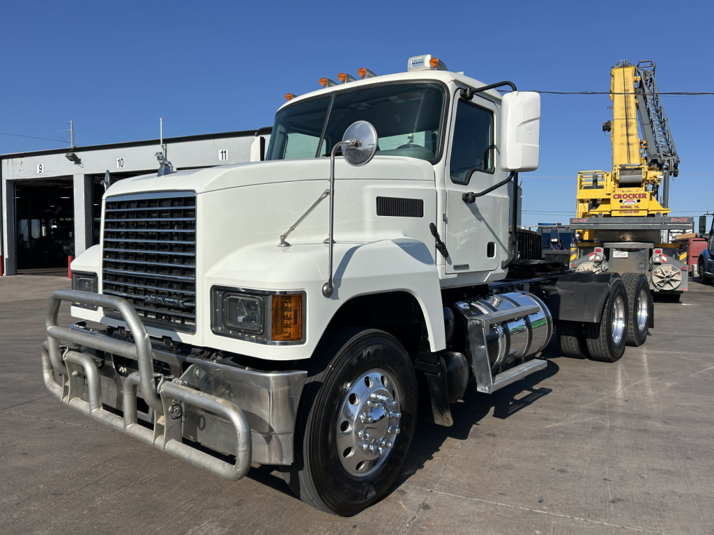Truck: 2020 Mack PI64T conventional daycab with front bull bar, dual round mirrors, mounted fuel tanks, and a heavy-duty crane in background.