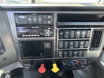 Mack PI64T dash showing gear shifter panel R N D P with M star buttons, radio/clock, empty stereo slot, climate controls, and red and yellow warning knobs.