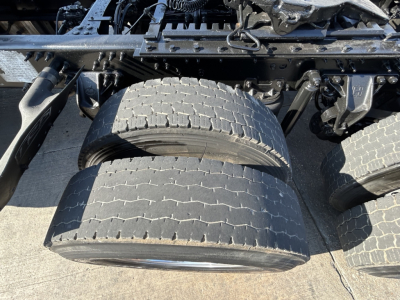 Truck wheel area showing dual rear axle tires on a Mack PI64T tractor, with visible frame, suspension components, and tire treads.