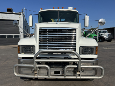 Front view of a white 2020 Mack PI64T truck showing a large chrome grille, two rectangular headlights, wide bumper with a heavy-duty bull bar, and side mirrors.
