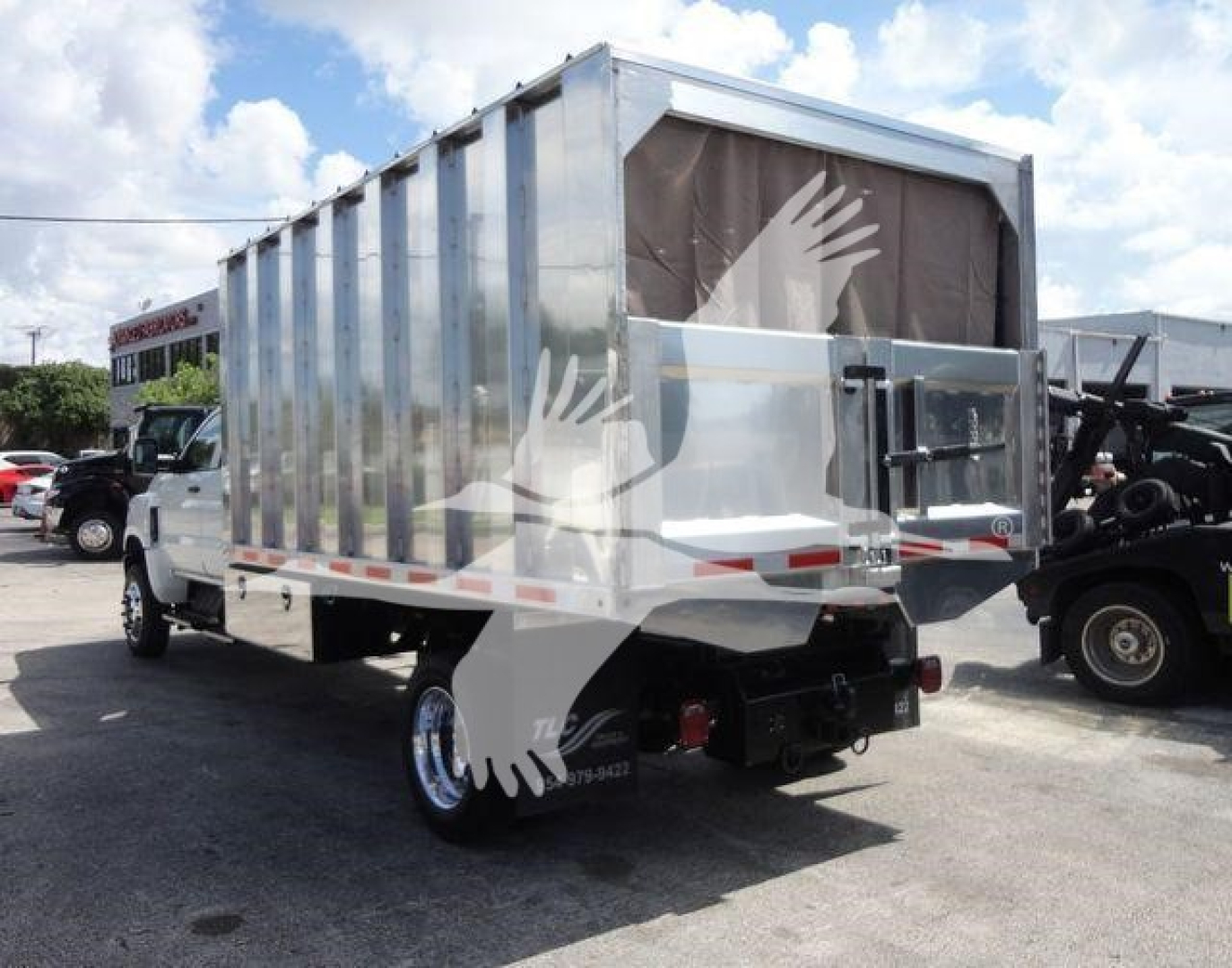 Dump truck in a dealership lot with metal-sided dump bed and white cab, side decals, rear view showing taillights and hitch