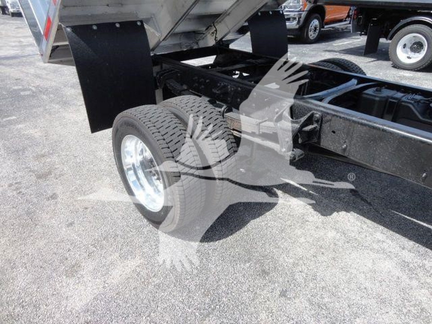 Dump truck chassis showing rear dual wheels and chassis frame with fifth wheel area visible and dump bed hinge; image focuses on rear left wheel and undercarriage.