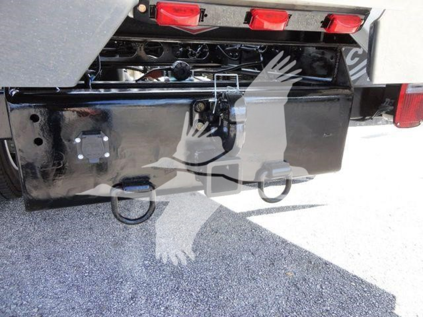 Truck rear showing bumper hitch and hydraulic components with black metal panel and red rear lights.