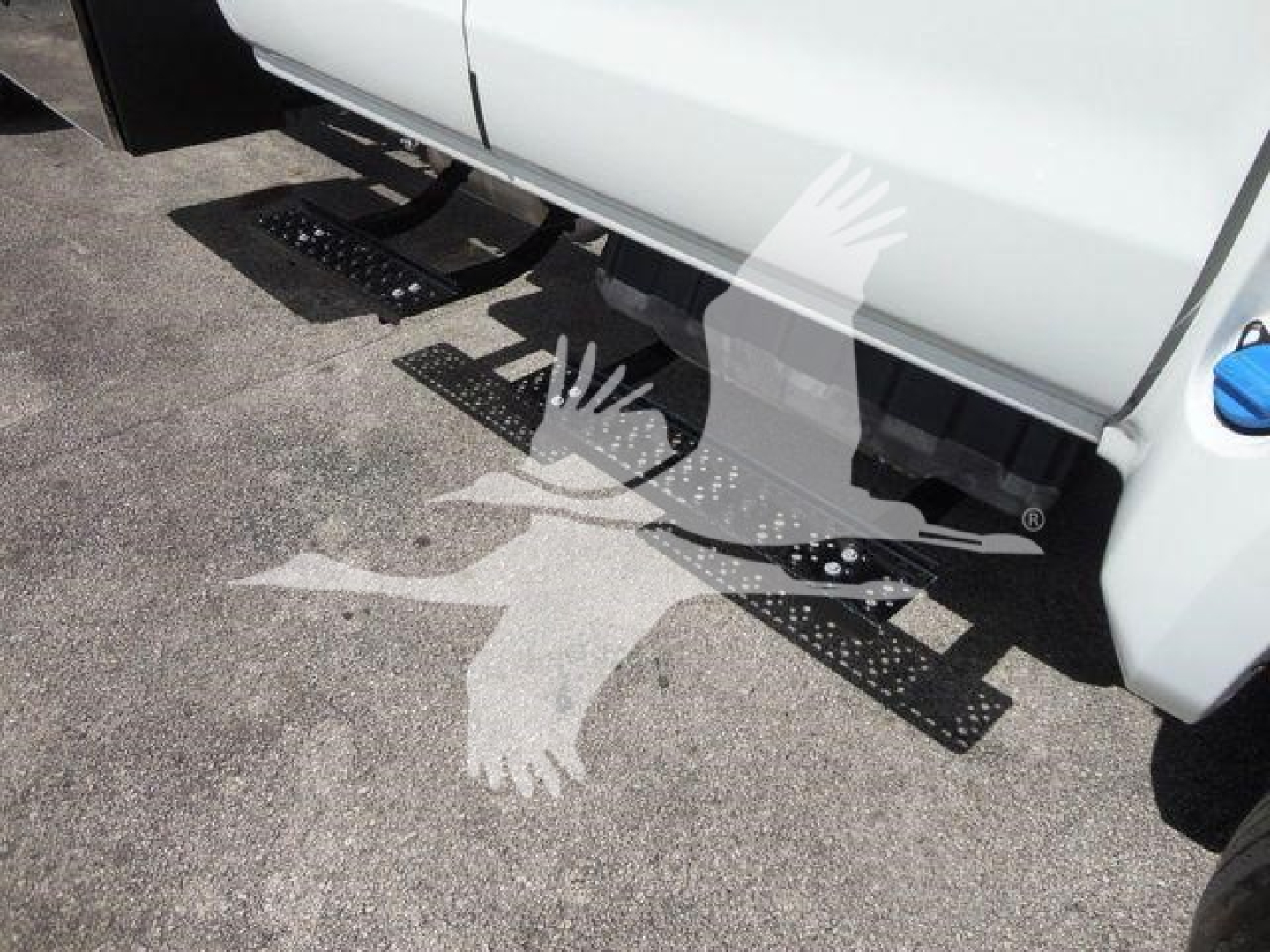 Truck side view showing a white cab and black metal steps beneath along the underside of the truck.