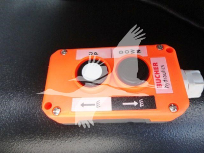 Orange Buicker hydraulics valve block with two control dials and arrows showing flow direction, mounted in a black surface.