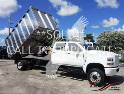 Truck with a raised dump bed on a white International CV chassis, side view showing hydraulic tilt mechanism and dual rear wheels.