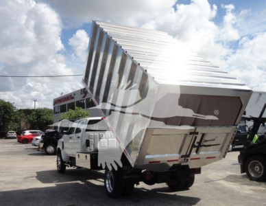 Truck with a dumping bed raised in a dealership lot showing a stainless steel dump body and International CV branding.