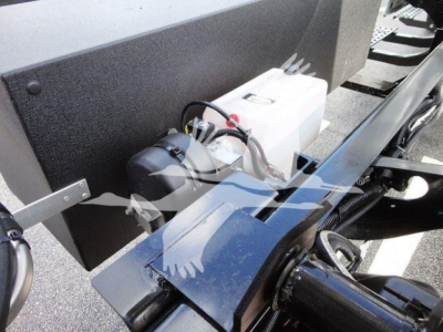Truck engine bay with white reservoir and black cylindrical component; wiring harness visible; metal frame and blue painted surface.