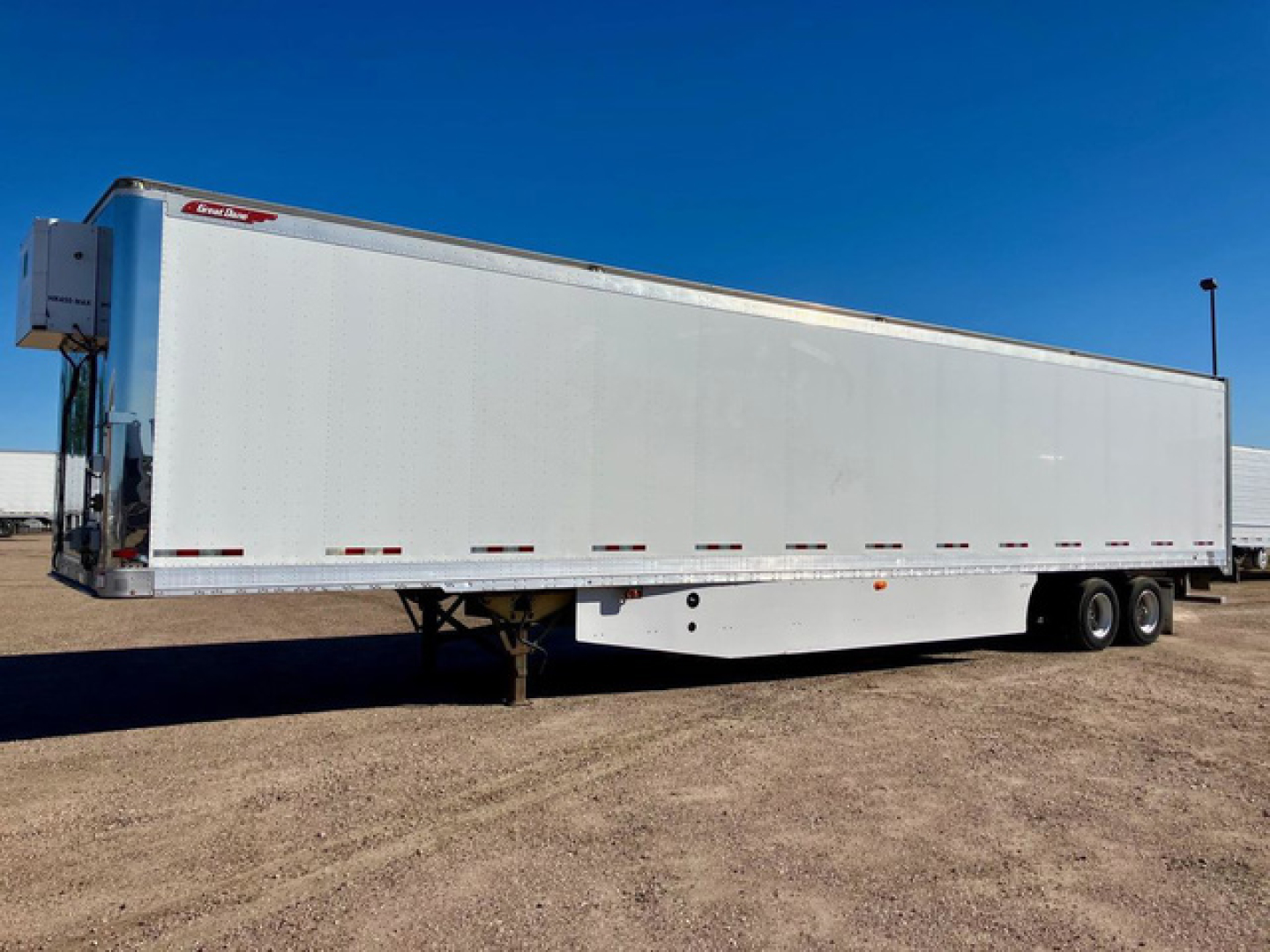 Great Dane dry van trailer side view showing long white rectangular cargo area, tandem axles, front landing gear, tractor hookup at front left, no visible branding aside from small Great Dane logo.