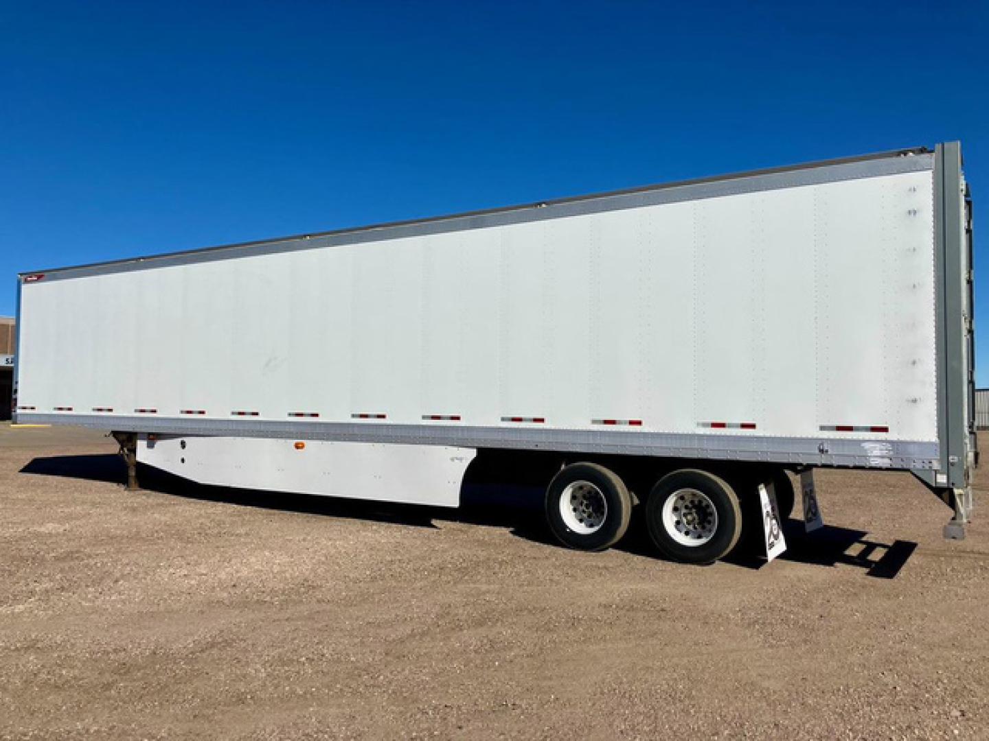 Trailer side view showing a white Great Dane dry van trailer with tandem axles and a flat dirt lot.