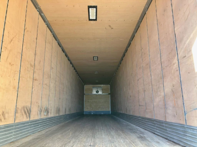Trailer interior showing wooden walls and metal side rails, empty cargo area with ceiling lights and a rear door, no labels visible.