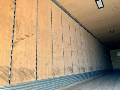 Trailer interior showing plywood sidewalls with metal channel uprights and a rubberized floor edge; no text visible.