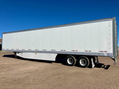 Trailer side view showing a white Great Dane dry van trailer with tandem axles and a flat dirt lot.