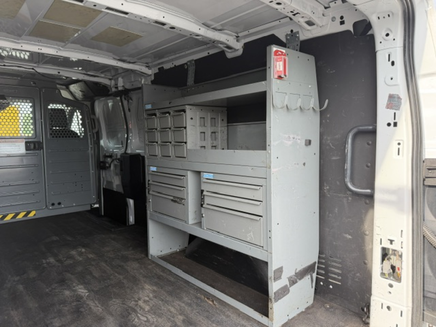 Ford Transit/Transit cargo van interior with steel service cabinet and tool drawers, metal shelving, and storage bins mounted along passenger side cargo area.