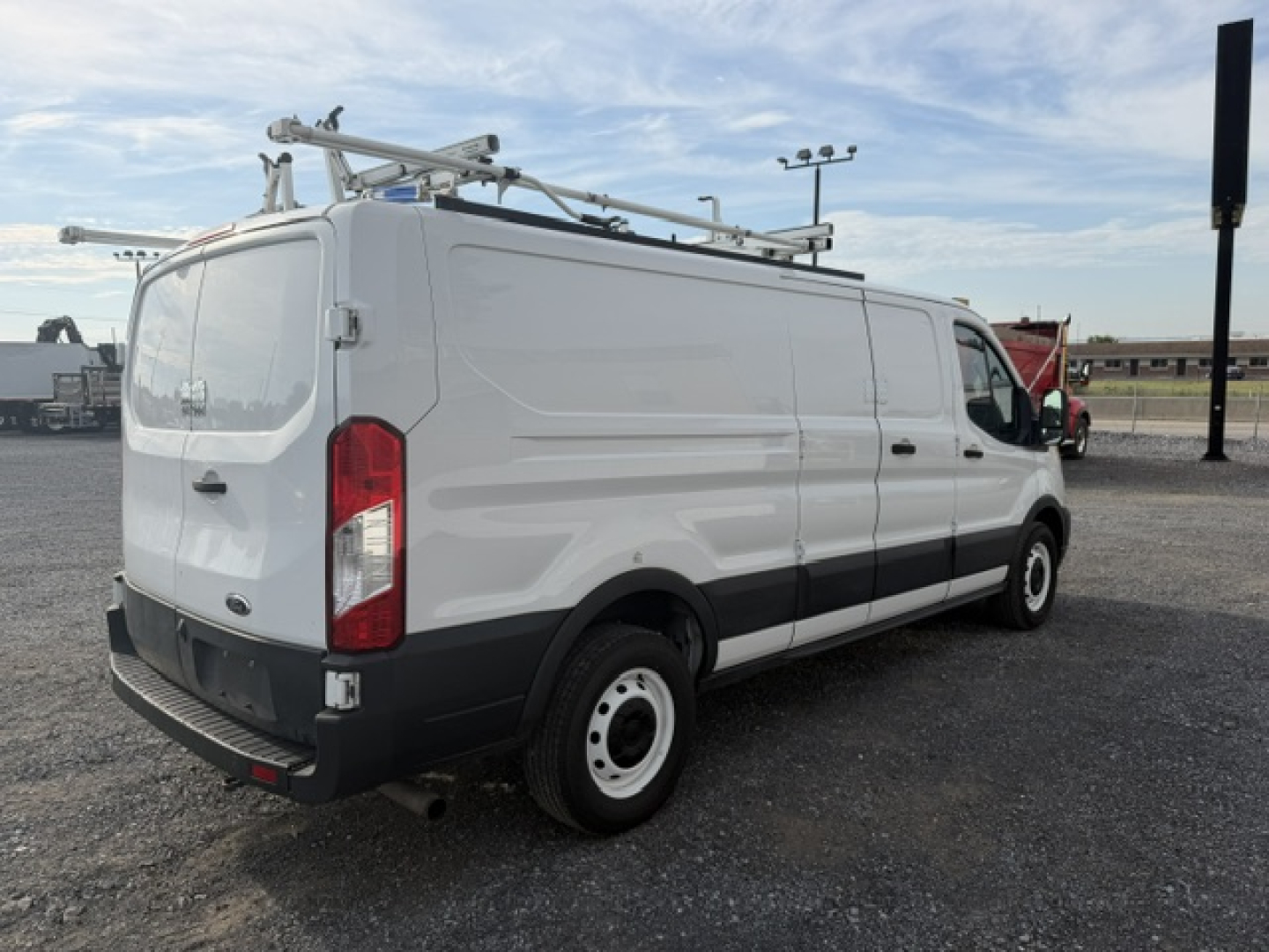 Ford TRANSIT/Transit-style utility van in service use with ladder rack on roof, rear doors, side profile visible.
