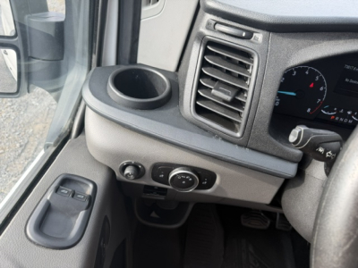 Vehicle interior showing driver-side dashboard with circular control knob, air vent, steering column, window switches, and cup holder.