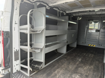Ford Transit/T-Series cargo van interior with metal shelving, wheel rack, and storage cabinets along the left side in a service utility truck.