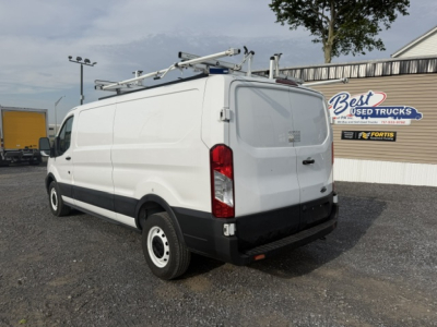Service/utility van with ladder rack on top, rear doors closed, Fortis used trucks sign in background; Ford Transit 250 badge faint on rear.