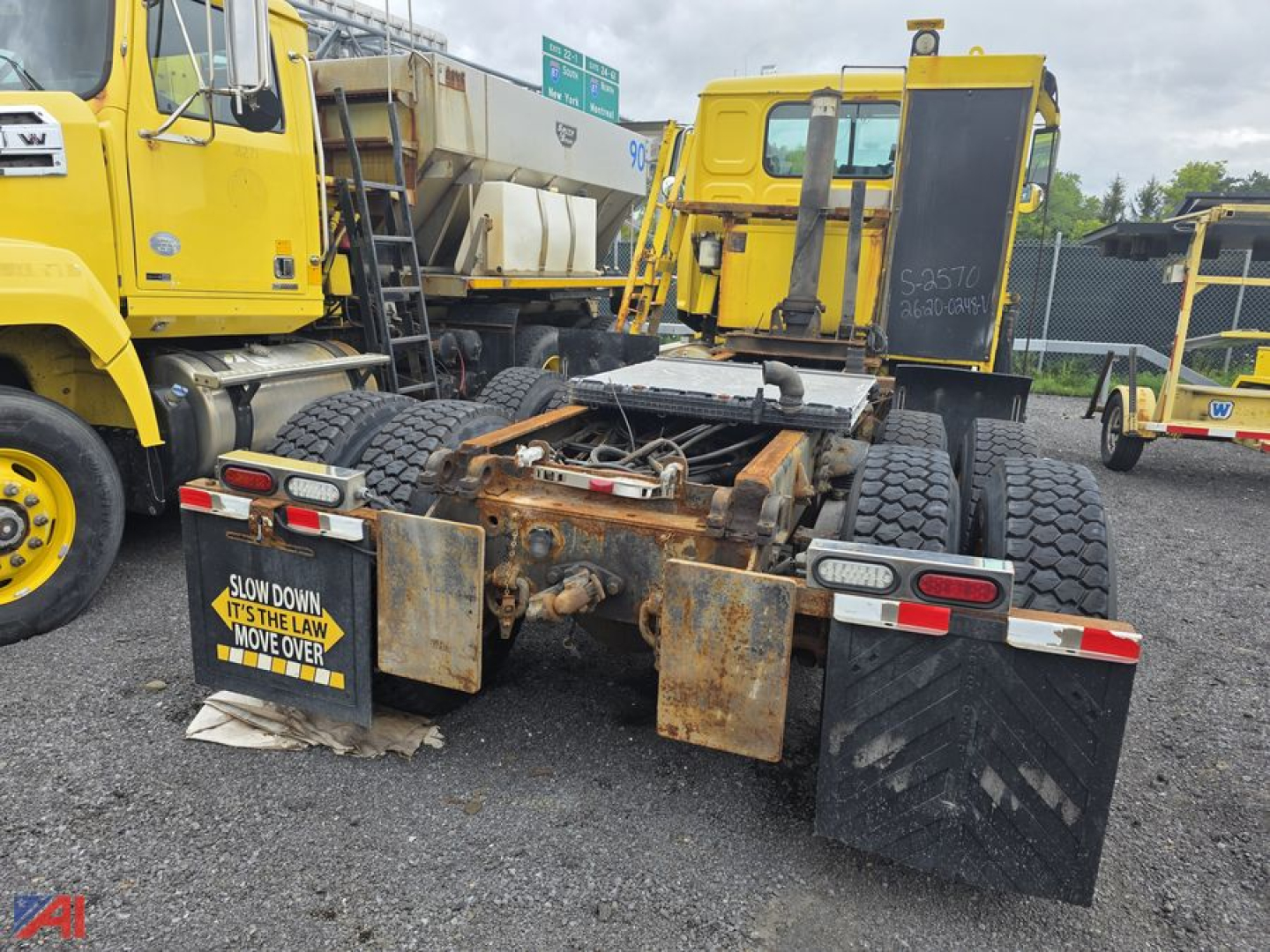 Rear view of a used 2014 Western Star 4700 SF cab and chassis showing dual rear axles, fifth wheel area, and bumper; rust on hitch area and mud flaps; yellow trucks in background.