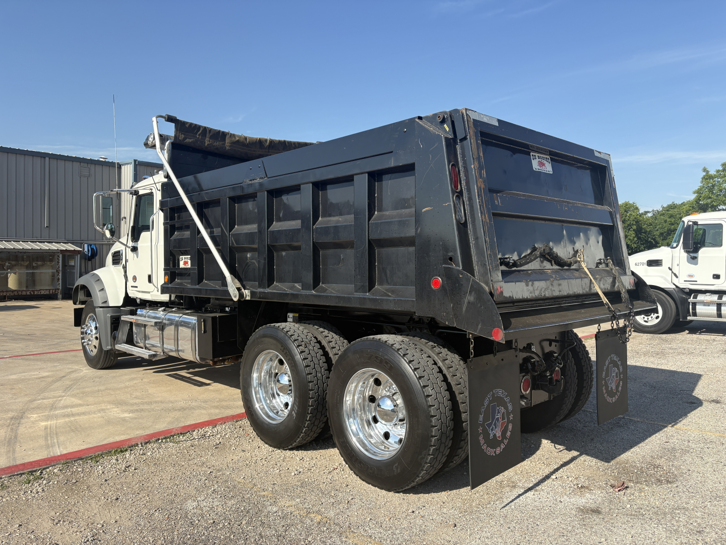 Dump truck rear and side view showing dual rear axles with black dump bed and mud flaps, metal rims, and tailgate with chain hooks.