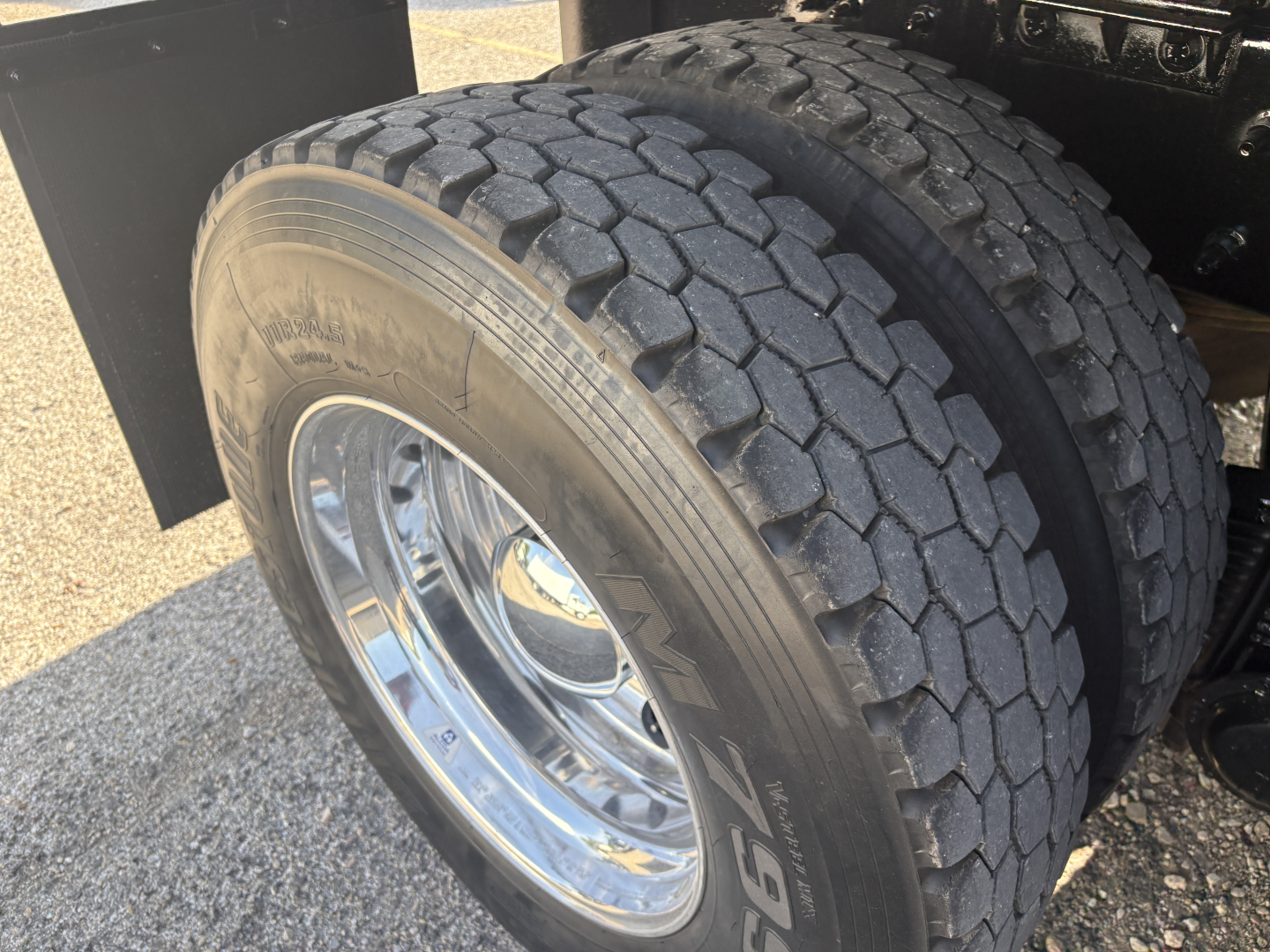 Truck dual rear axle tire close-up showing heavy-duty tread and chrome wheel; part of Mack GR64F dump truck undercarriage.
