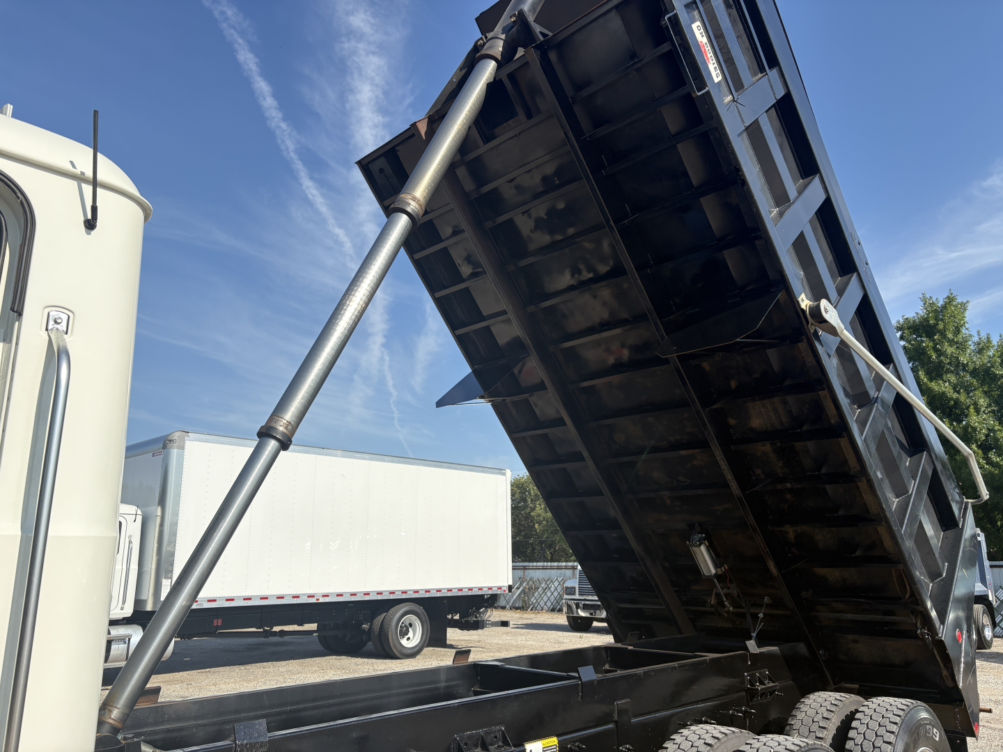Mack GR64F dump truck bed in raised position showing hydraulic cylinder and underside of bed with black steel panels.