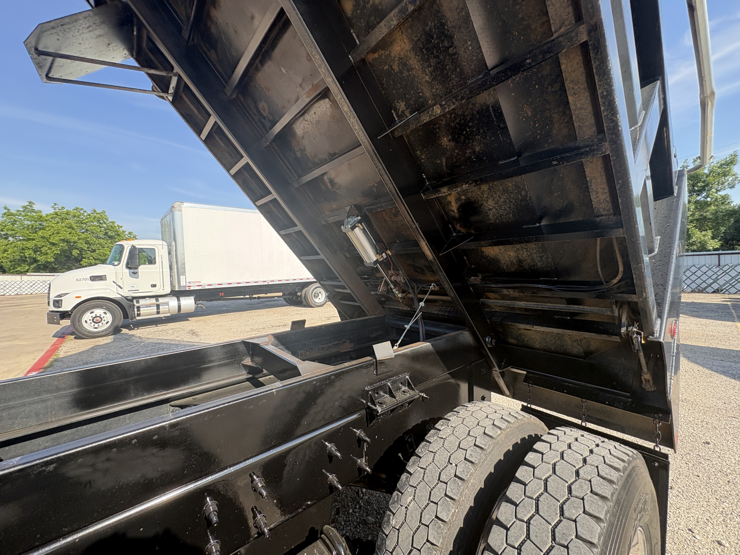 Dump truck bed raised showing hydraulic mechanism and dual rear wheels on a Mack GR64F chassis.