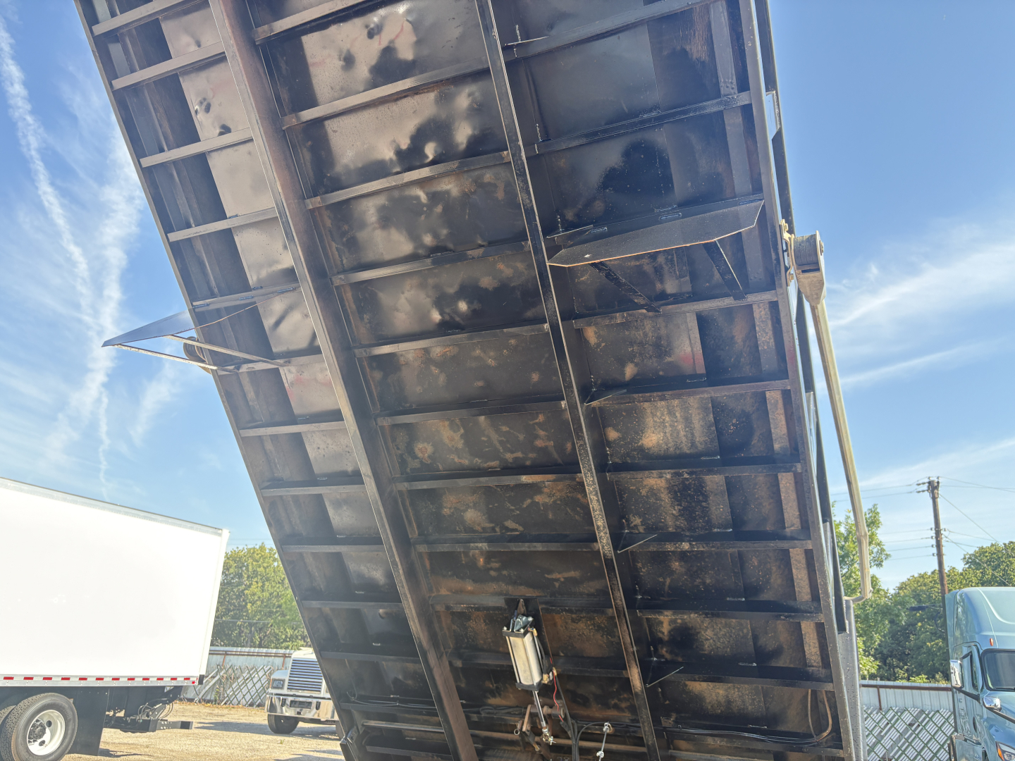 Dump truck bed underside showing metal frame and hydraulic mechanism in view, grime on surfaces.