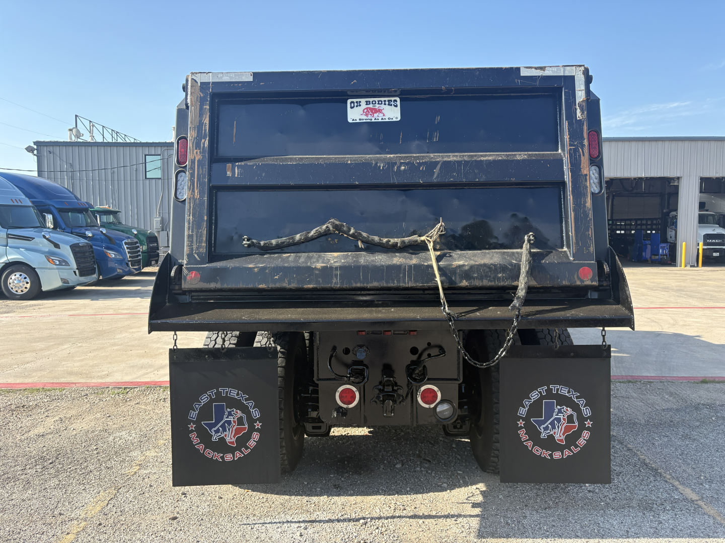 Dump truck rear showing mud flaps with star logo, tailgate, and rear underride hitch area. Visible components include two rear lights, license plate area, and chained tailgate support.