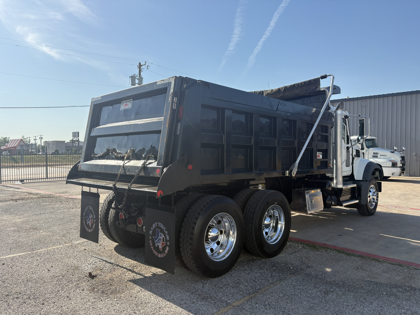 Dump truck rear three-quarter view showing dual rear axles and dump bed with hydraulic system and mud flaps.