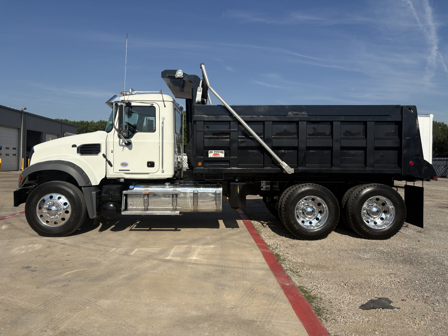 Truck side view of a Mack GR64F dump truck with a white cab and black dump bed.