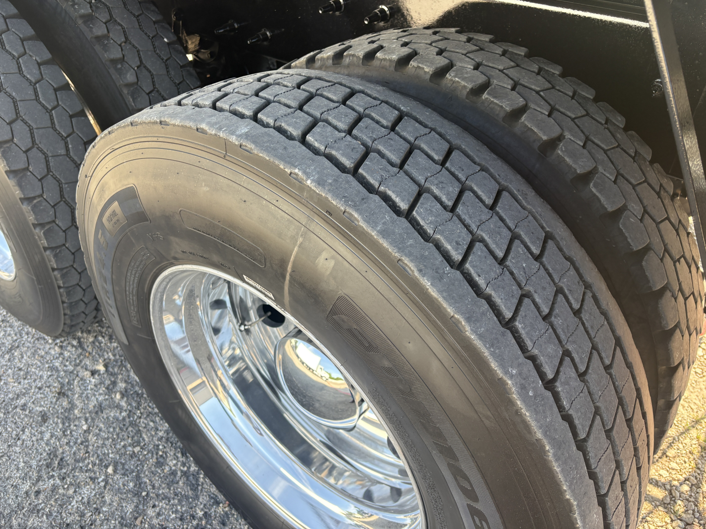 Truck tire and dual rear wheel setup visible in the wheel well of a Mack GR64F dump truck. Tire tread pattern clear with chrome rims.