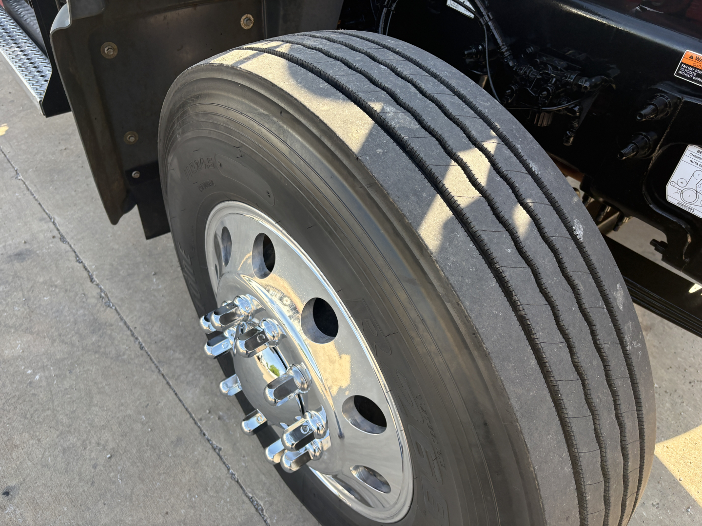 Truck front wheel of a 2025 Mack GR64F dump truck showing a single front dual rear? Actually image shows front dual? It shows a single front axle wheel with large drum? Type: wheel and tire with lug nuts and chrome hub.