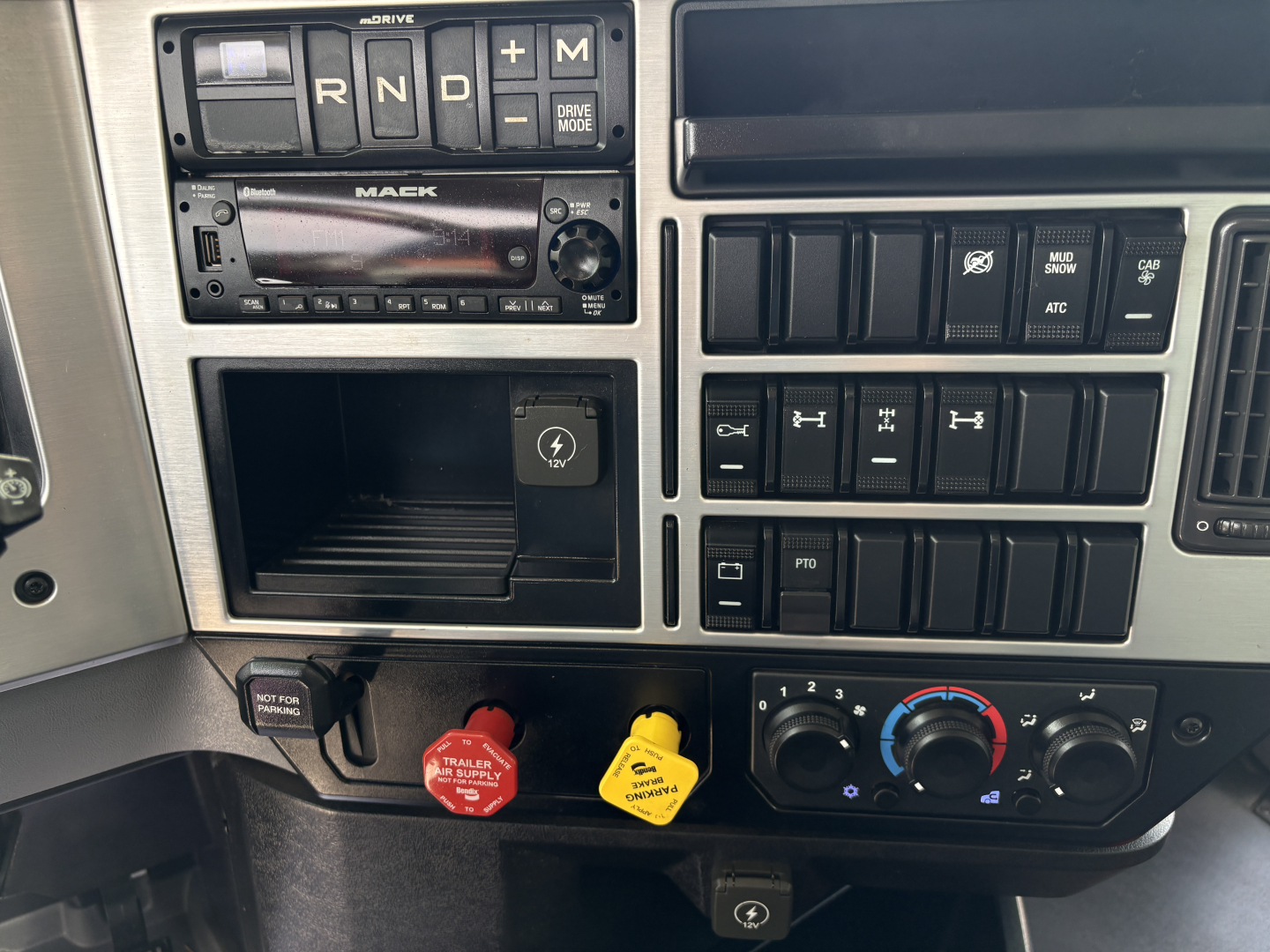 Mack GR64F interior driver-side dash showing gear selector (R N D L), engine start switch, radio, control switches, red and yellow trailer air switches, and climate controls.
