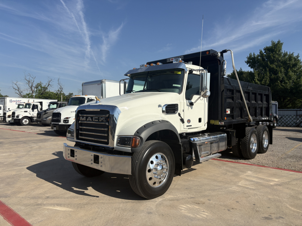 Mack GR64F dump truck in a parking lot, white cab, black dump body, front grille with Mack emblem, dual rear axles.
