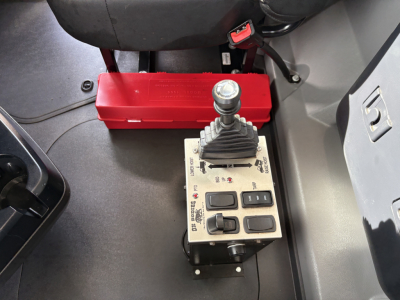 Cab interior showing a gray joystick-style gear/controls with multiple buttons and a red battery box nearby.