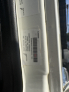 View of a vehicle door jamb with a white label containing barcodes and text.