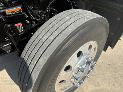 Truck wheel showing dual rear tires with polished aluminum wheel and lug nuts, undercarriage components visible; tire tread and sidewall details.